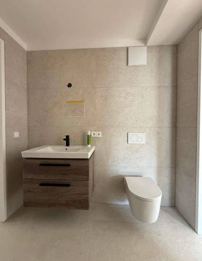 Modernes Badezimmer mit schwebendem Waschtisch, wandhängendem WC und großformatigen Fliesen.