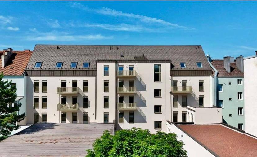 Modernes Mehrfamilienhaus mit Balkonen und Dachfenstern in städtischer Umgebung.