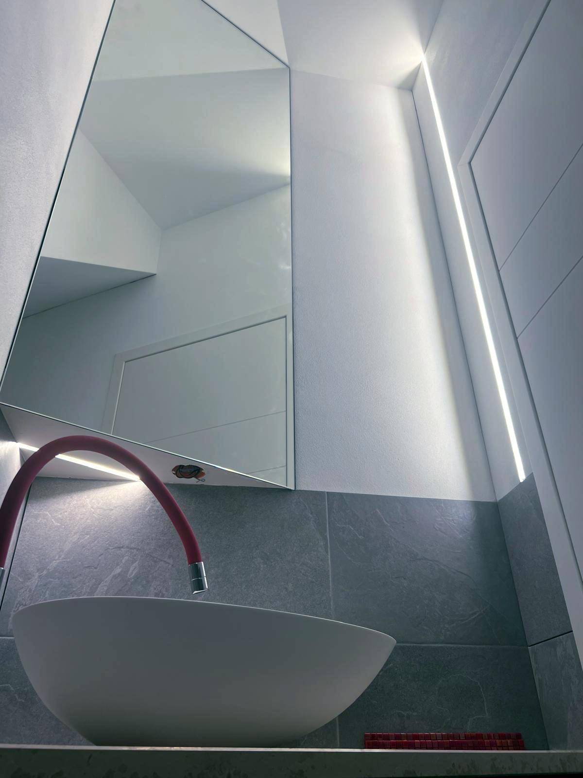 Modernes Badezimmer mit einzigartigem Spiegeldesign, Aufsatzwaschbecken und indirekter Beleuchtung.