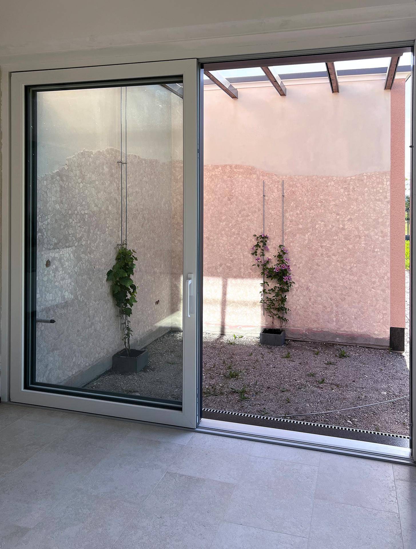 Blick von innen auf einen kleinen Außenbereich mit Pergola und Pflanzen durch große Schiebetüren.