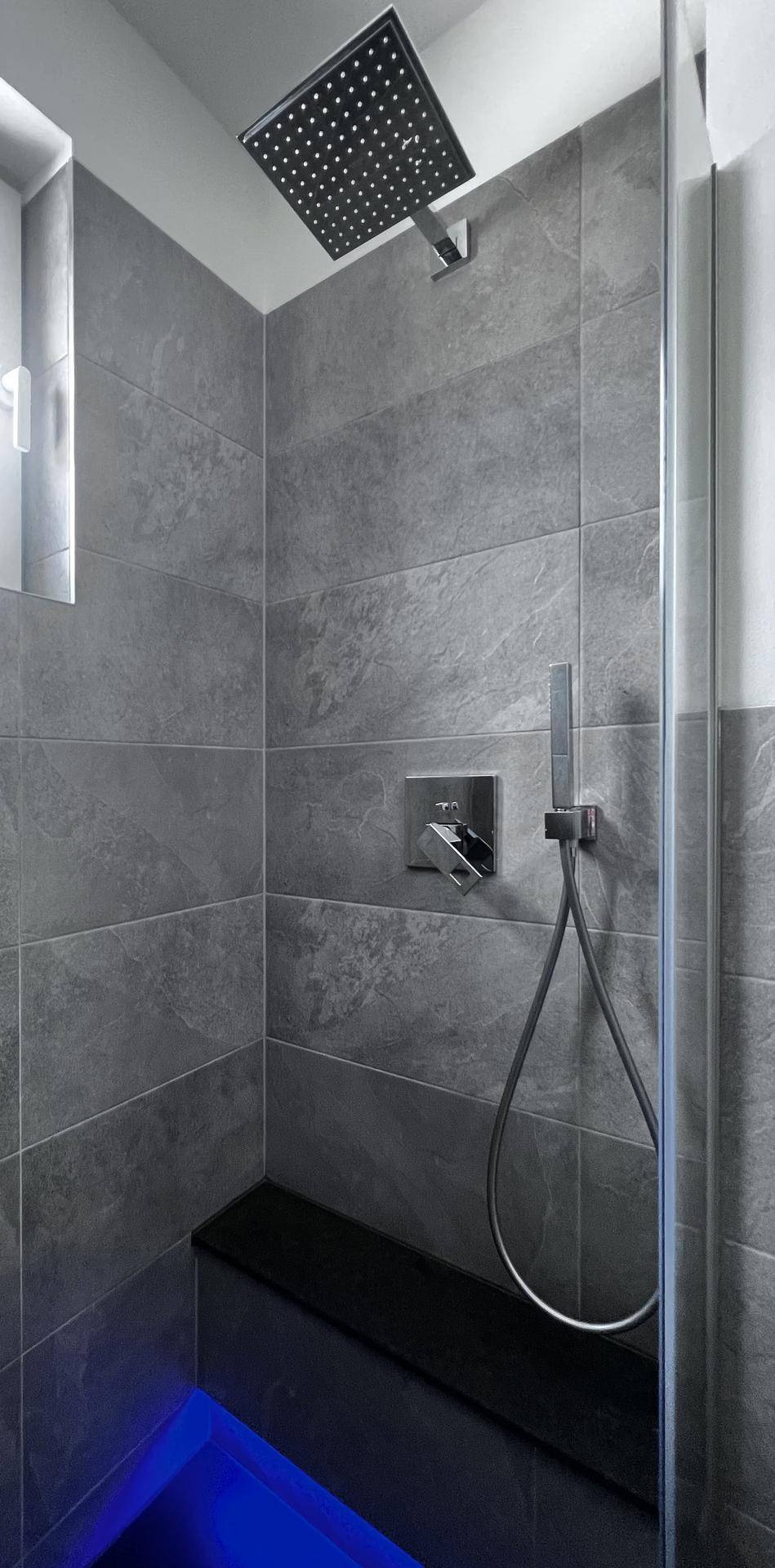 Begehbare Dusche mit Regenduschkopf, grauen Fliesen und integrierter Sitzbank.