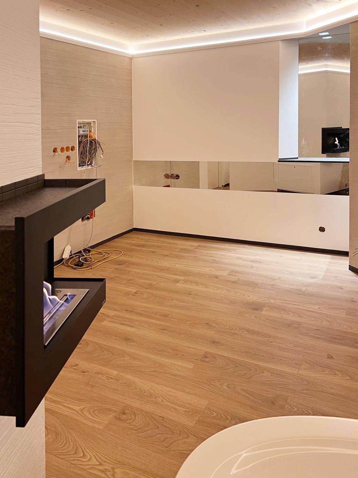 Heller Raum mit Holzboden, indirekter Deckenbeleuchtung und modernem Kamin.