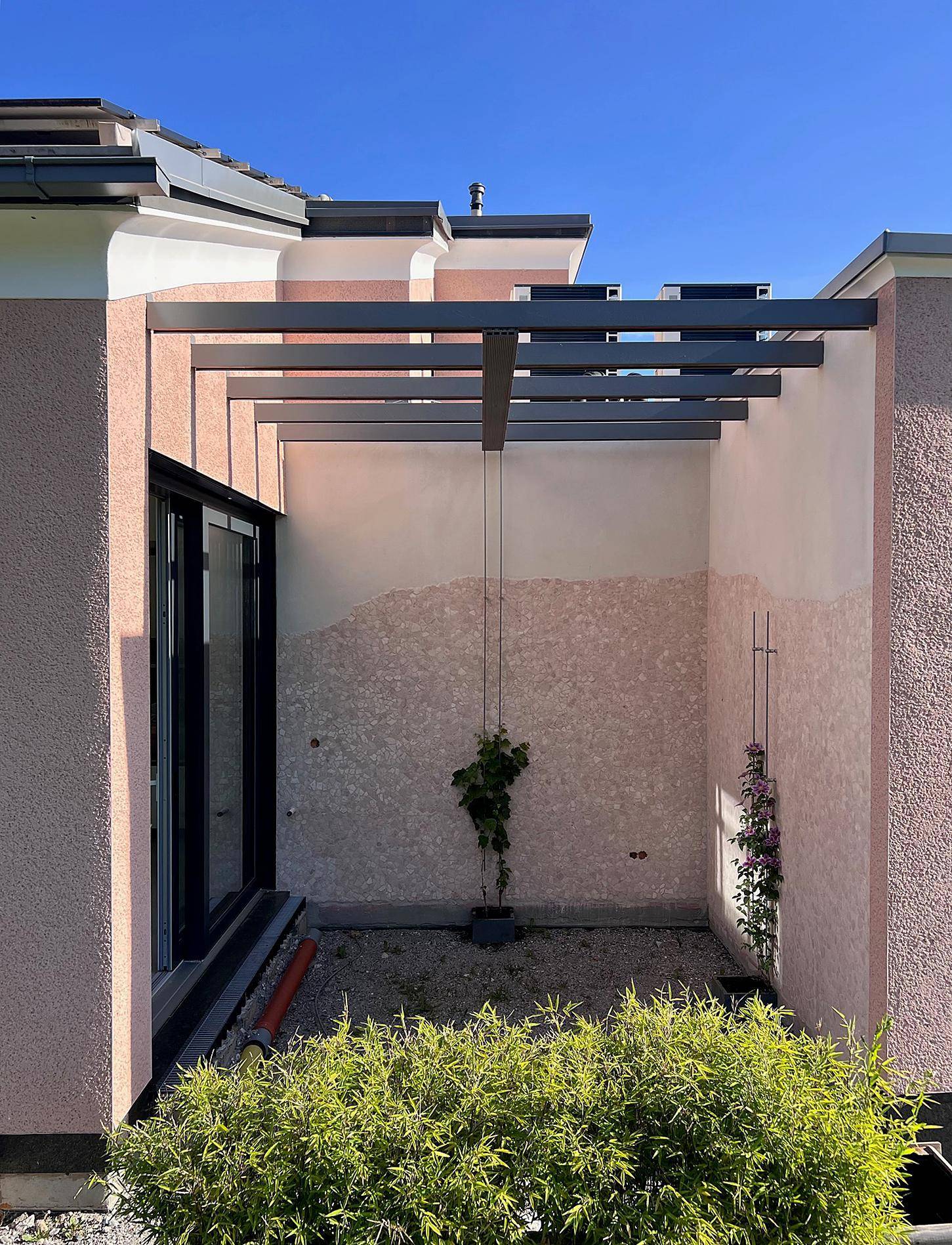 Außenbereich mit Pergola, bepflanztem Kiesbeet und moderner Fassadengestaltung.