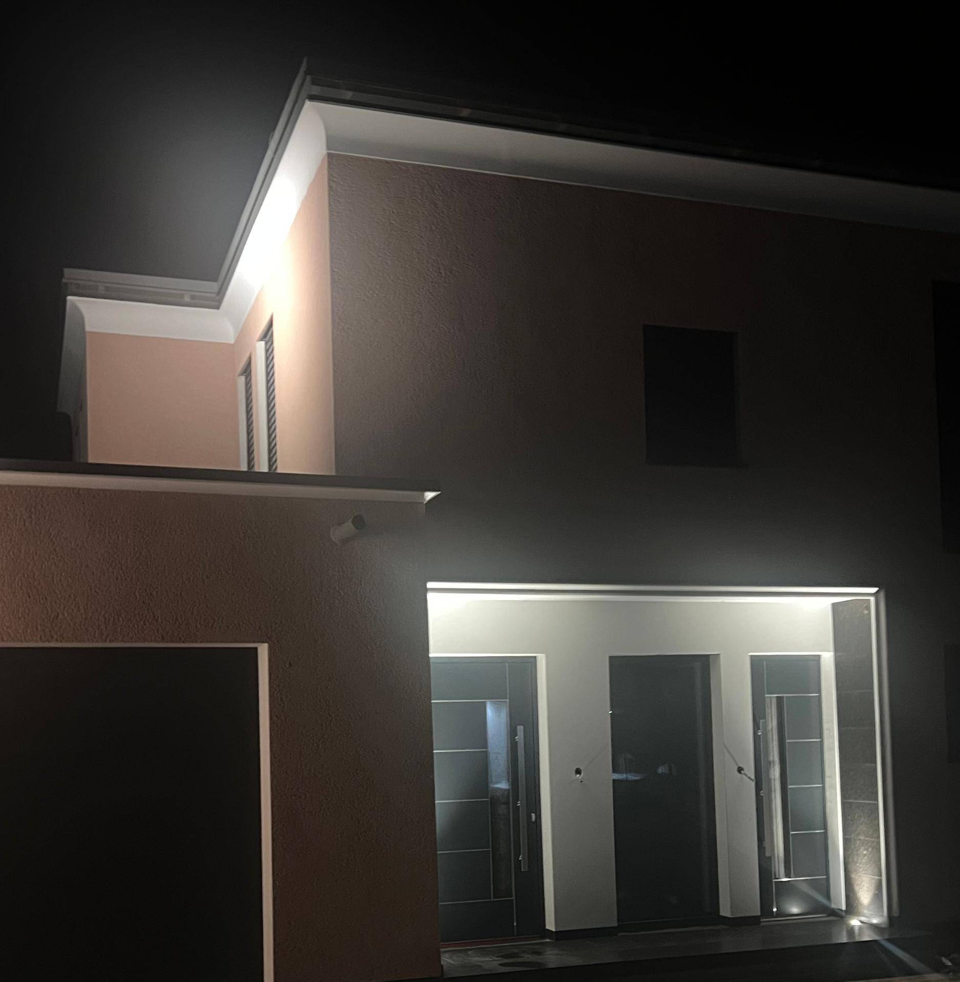 Beleuchteter Eingangsbereich eines modernen Hauses mit dunklen Türen bei Nacht.