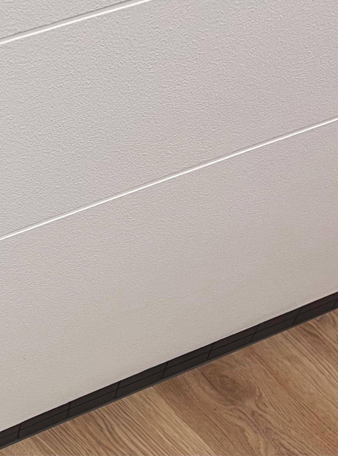 Nahaufnahme einer weißen Wand mit horizontalen Linien und Holzboden.