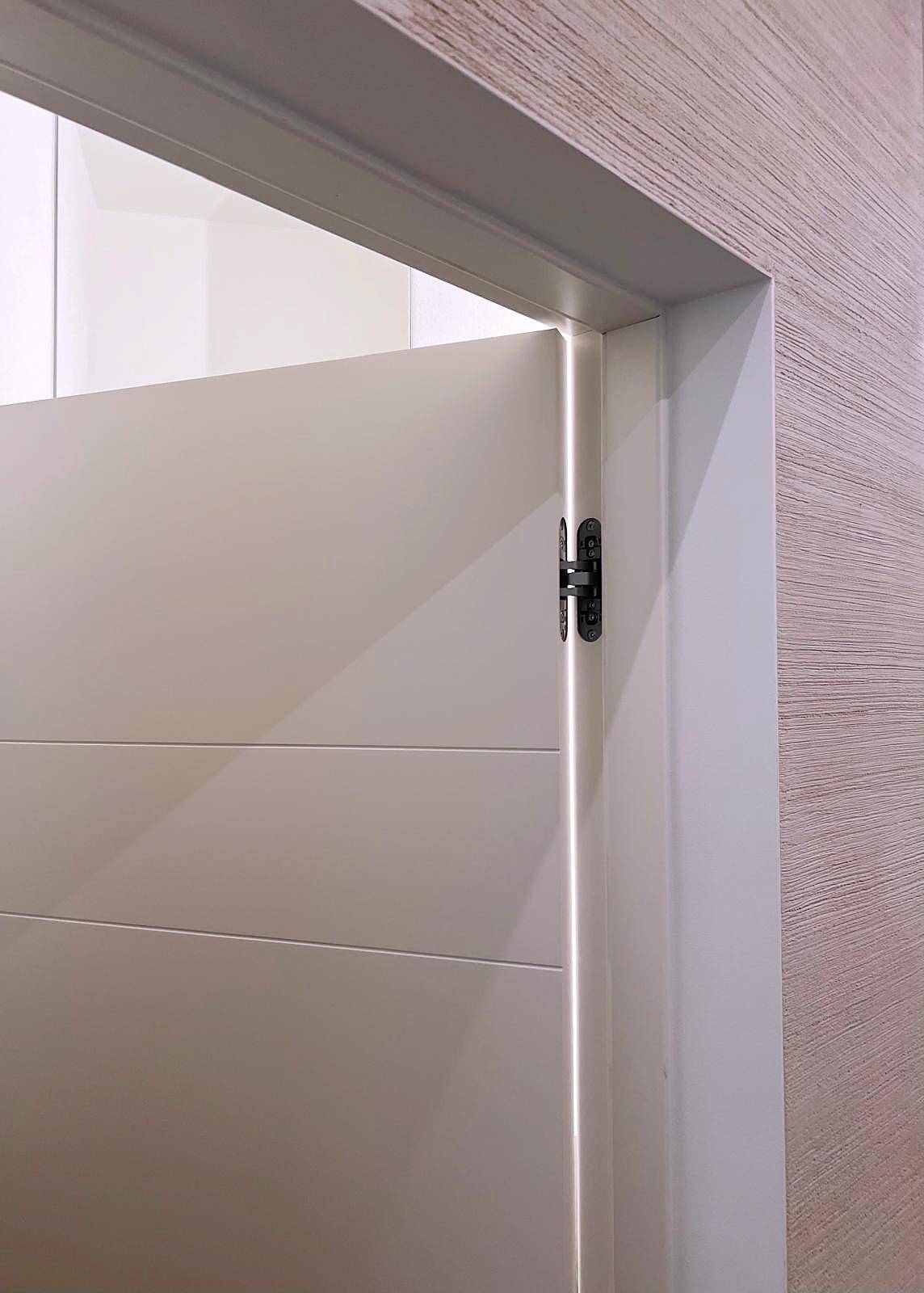 Detailansicht einer modernen weißen Tür mit sichtbaren Scharnieren und Holzrahmen.