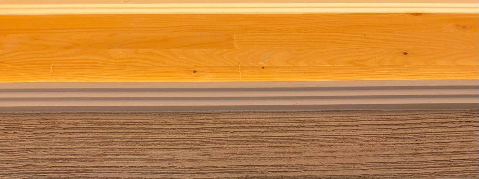 Nahaufnahme von Holzboden, einer Zierleiste und einer strukturierten Wandfläche.