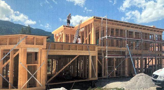 Holzrahmenbau eines modernen Hauses im Bau mit Arbeitern auf dem Dach und Gerüst.
