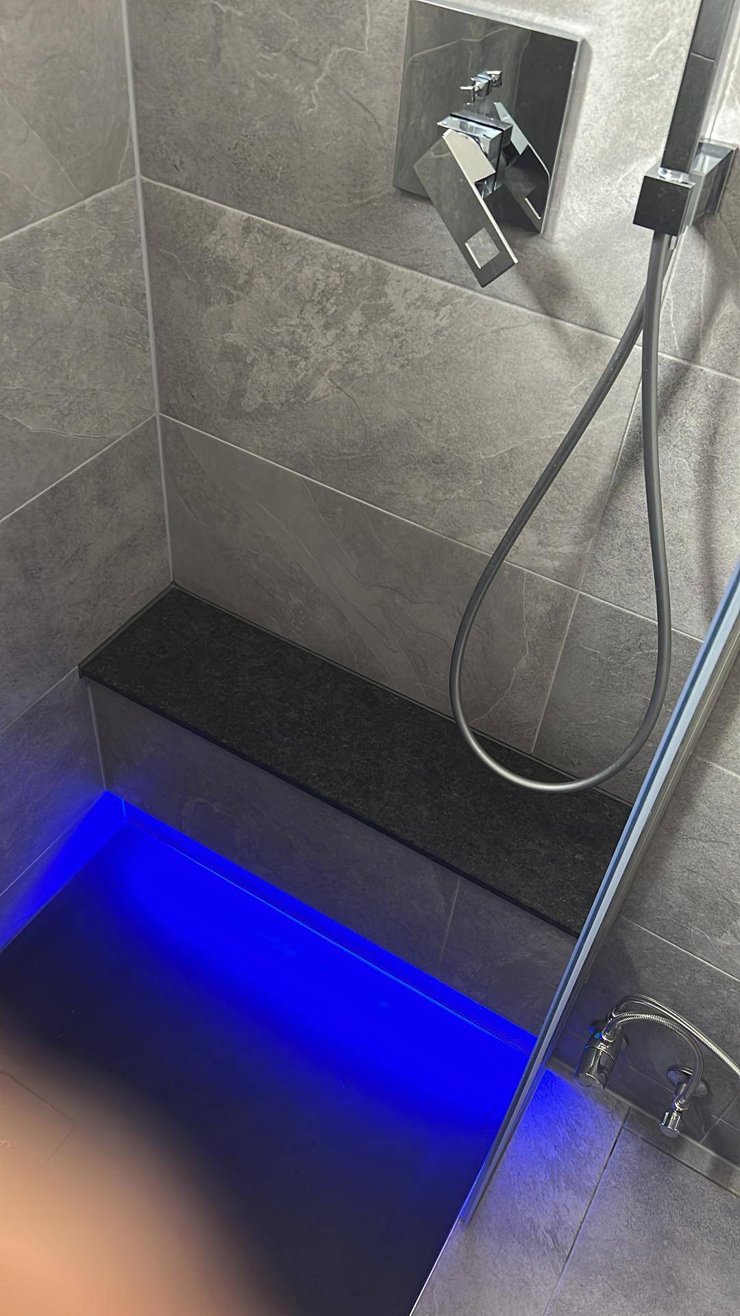 Detailansicht einer modernen Dusche mit blauer Bodenbeleuchtung und grauen Fliesen.