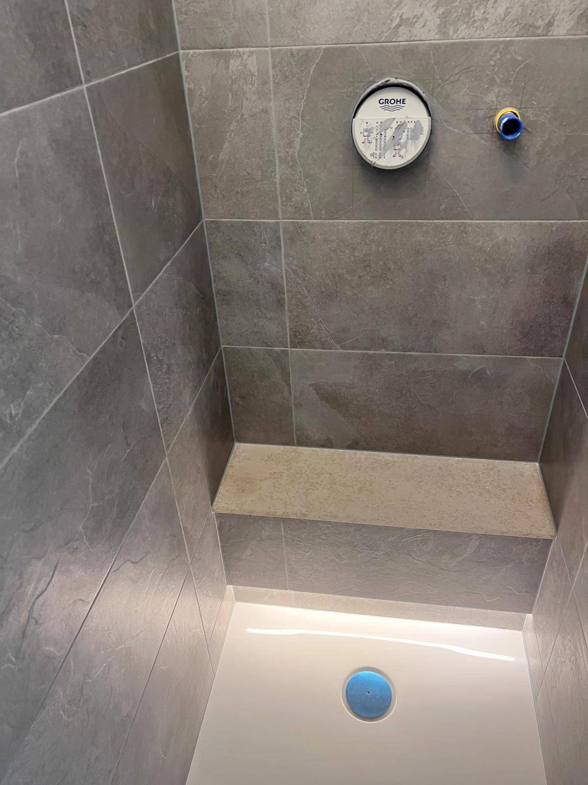 Moderne begehbare Dusche mit grauen Fliesen und integrierter Sitzbank.