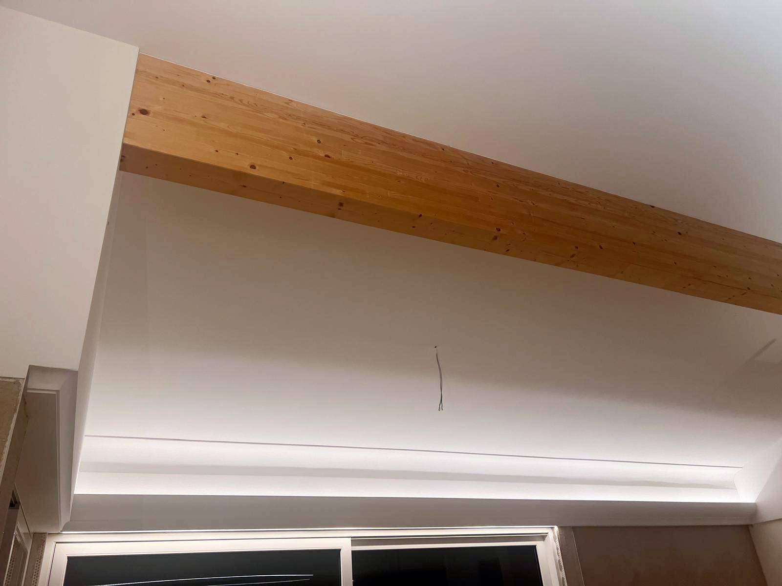 Decke mit sichtbarem Holzbalken und integrierter indirekter Beleuchtung in einem modernen Raum.