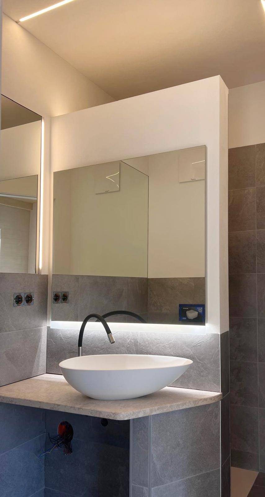 Modernes Badezimmer mit Aufsatzwaschbecken, großem Spiegel und grauen Fliesen.