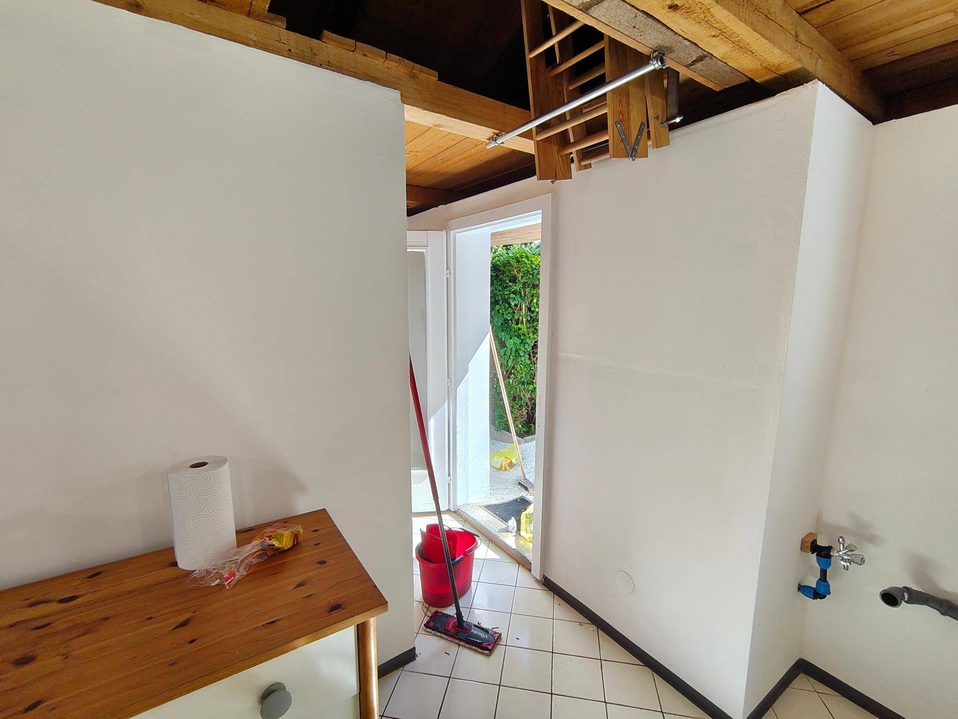 Innenraum eines Hauswirtschaftsraums mit Fliesenboden, Holzbalkendecke und Zugang zum Außenbereich.