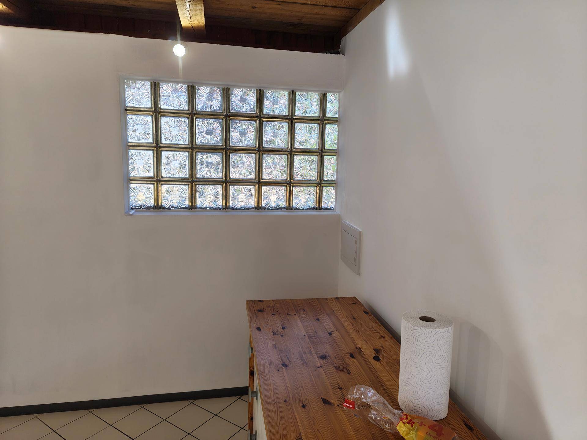 Innenraum mit großer Glasbausteinwand, Fliesenboden und einer einfachen Holzablage.