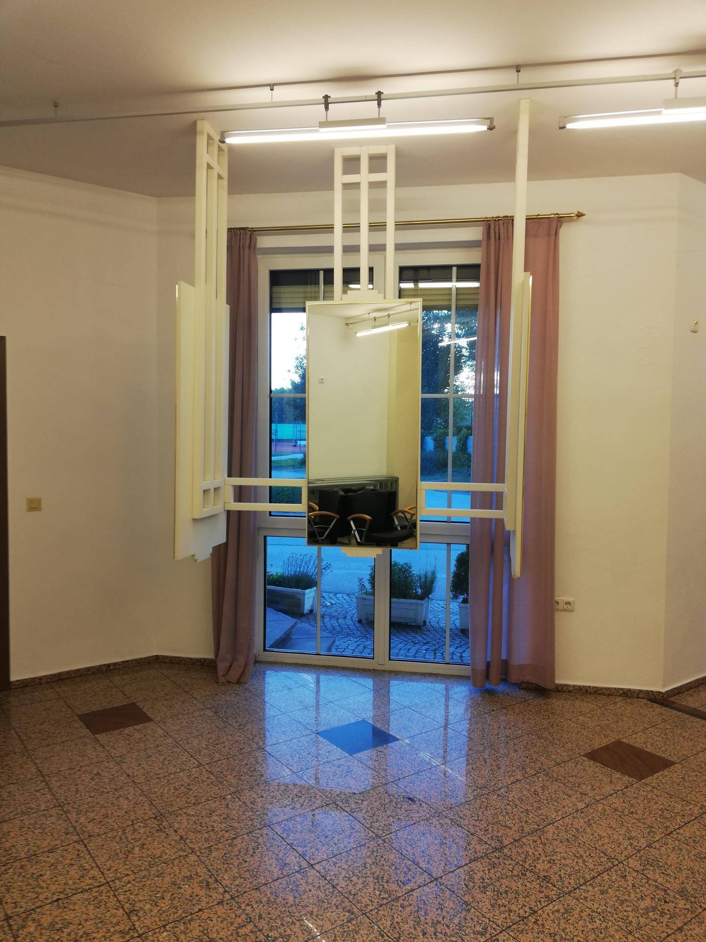 Geräumiger Gewerberaum mit großen Fenstern, gemustertem Fliesenboden und einer dekorativen Spiegeleinheit.