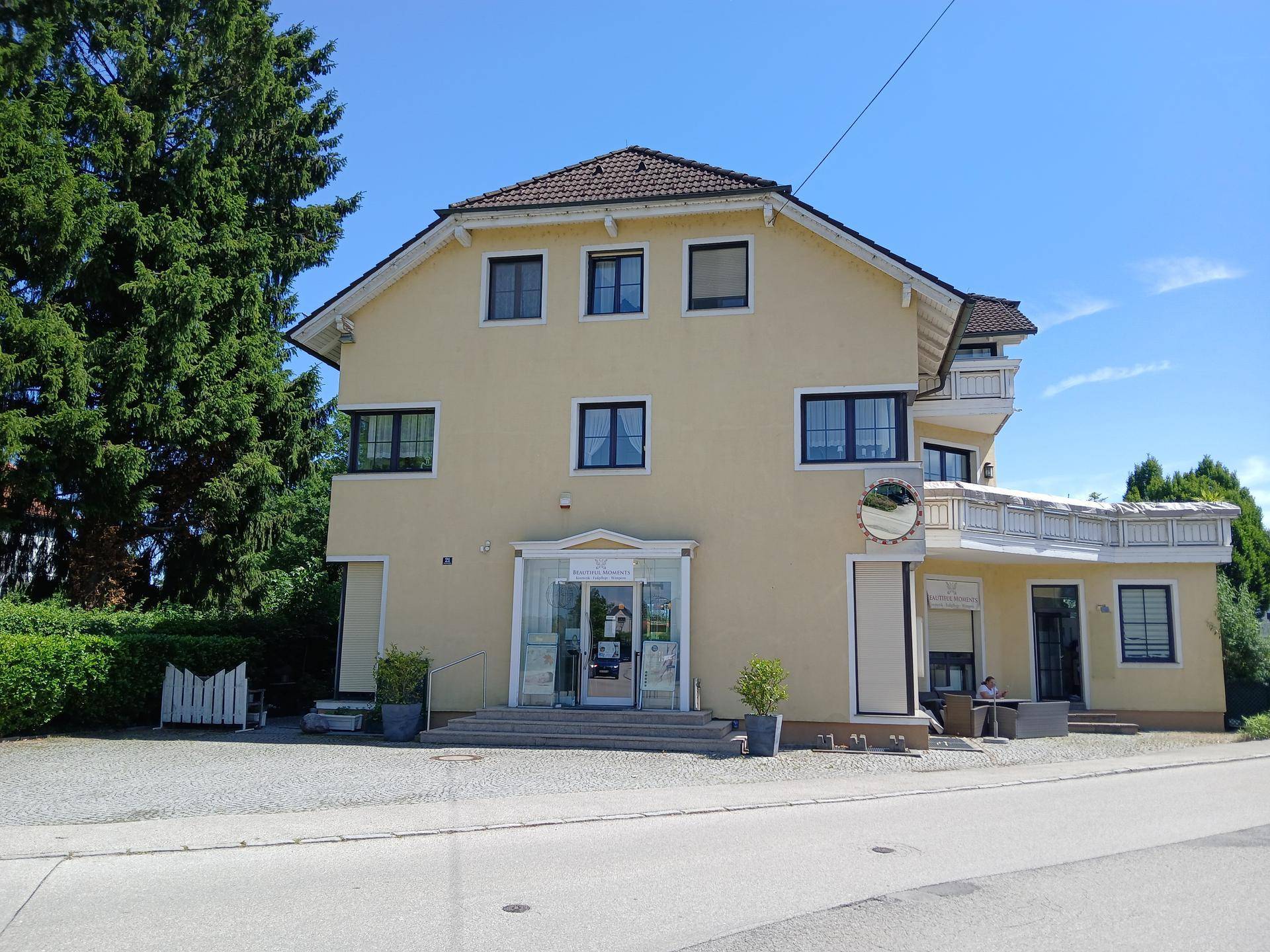 Gesamtansicht des gelben Gebäudes mit Balkon, umgeben von üppigem Grün und einer ruhigen Straße.