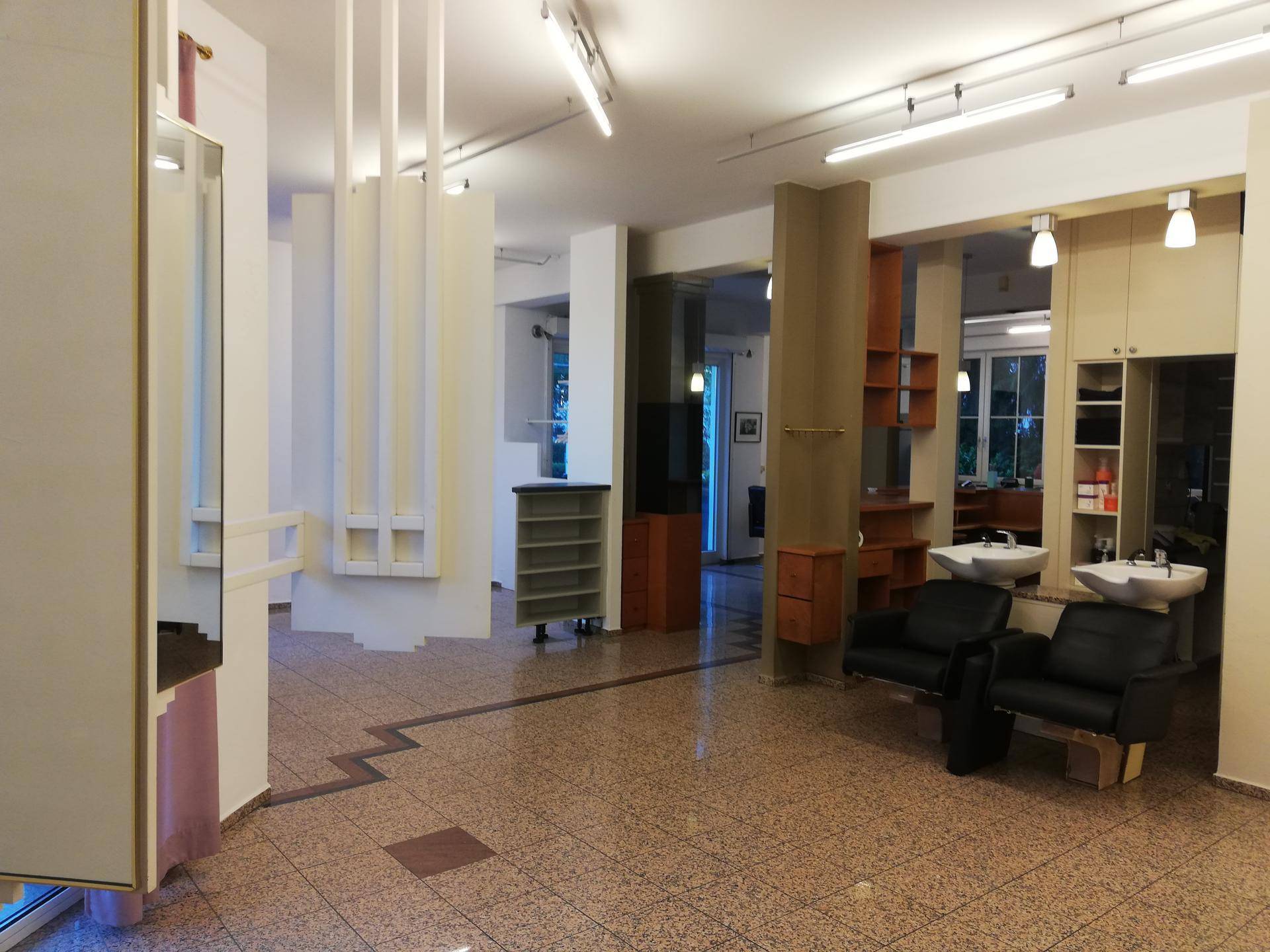 Großer Friseursalon mit mehreren Arbeitsbereichen, Waschbecken und Regalen, gut beleuchtet.