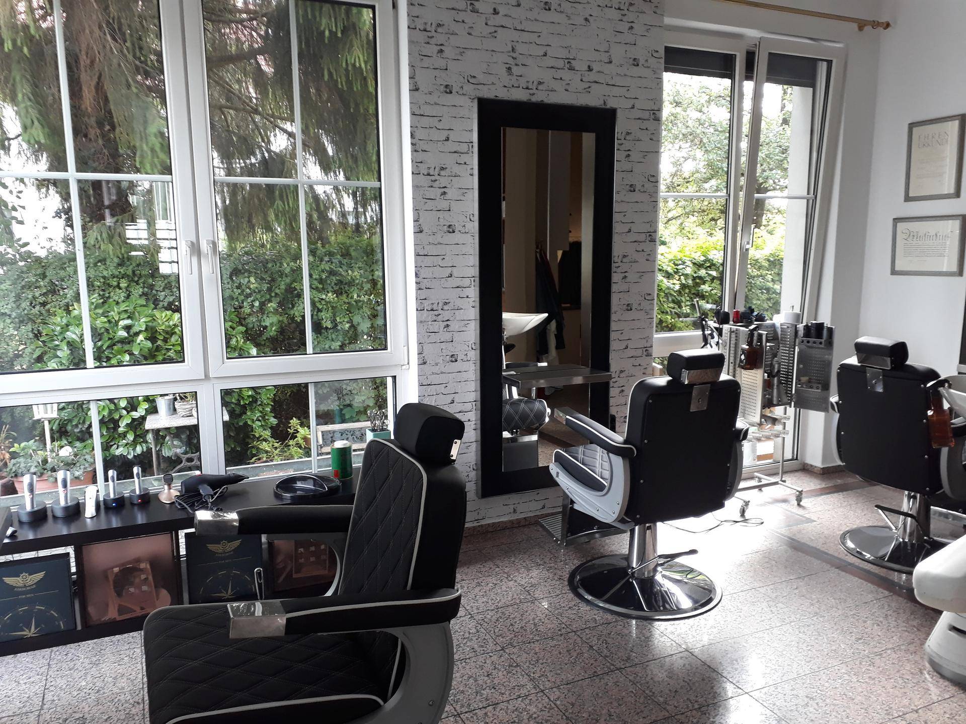 Heller Friseursalon mit großen Fenstern, Styling-Stühlen und einer Ziegelwand-Optik.