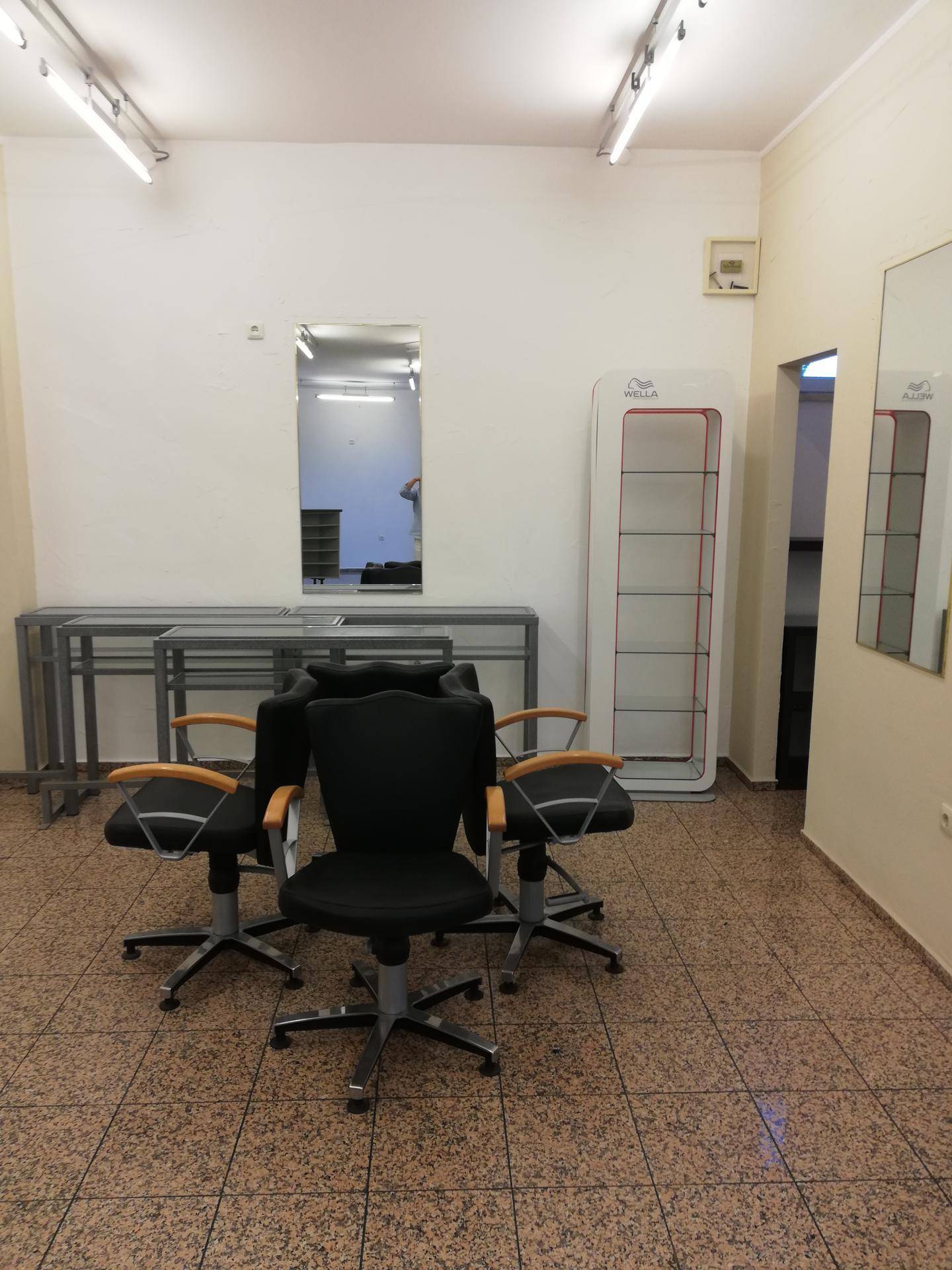 Friseursalon-Bereich mit mehreren Styling-Stühlen, einem Produktregal und Wandspiegeln.