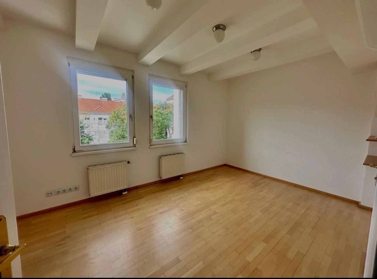 Helles Zimmer mit Holzboden, zwei Fenstern und Blick auf die Umgebung.