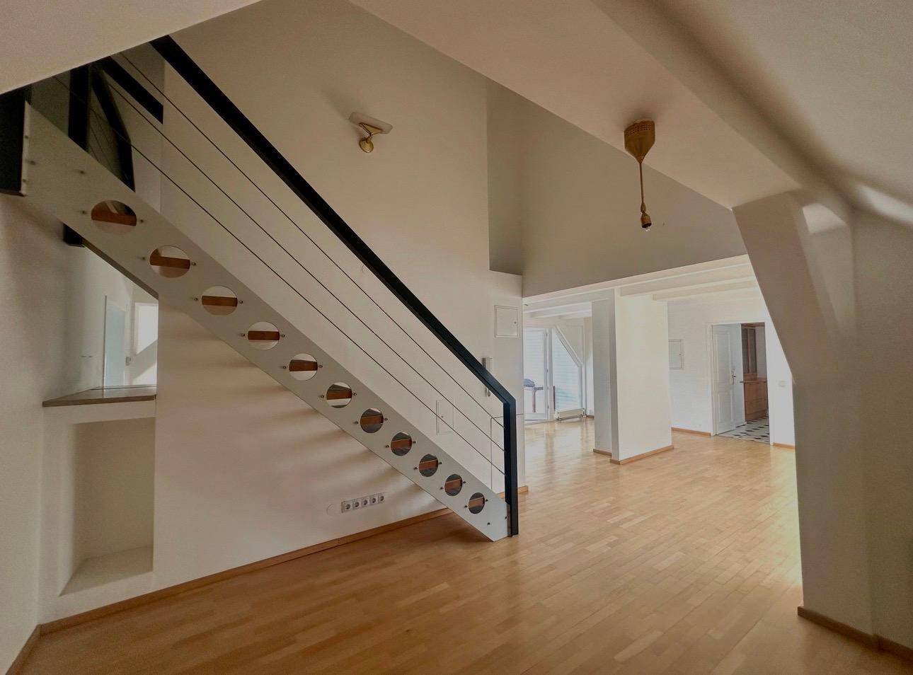 Offener Wohnbereich mit moderner Treppe, Holzboden und hohen Decken.