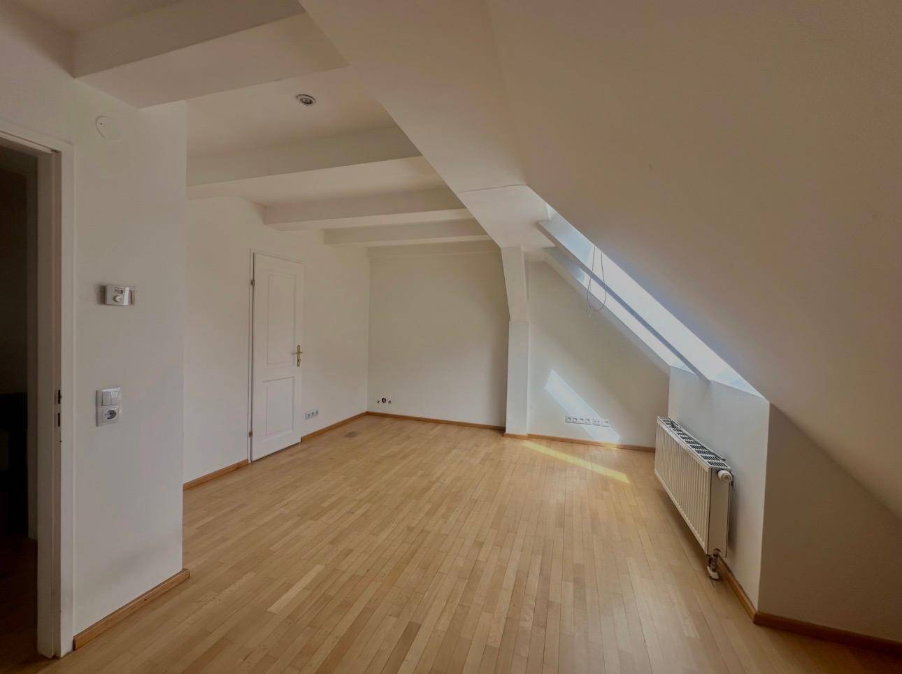 Heller Raum mit Holzboden, Dachschräge und sichtbaren Deckenbalken.