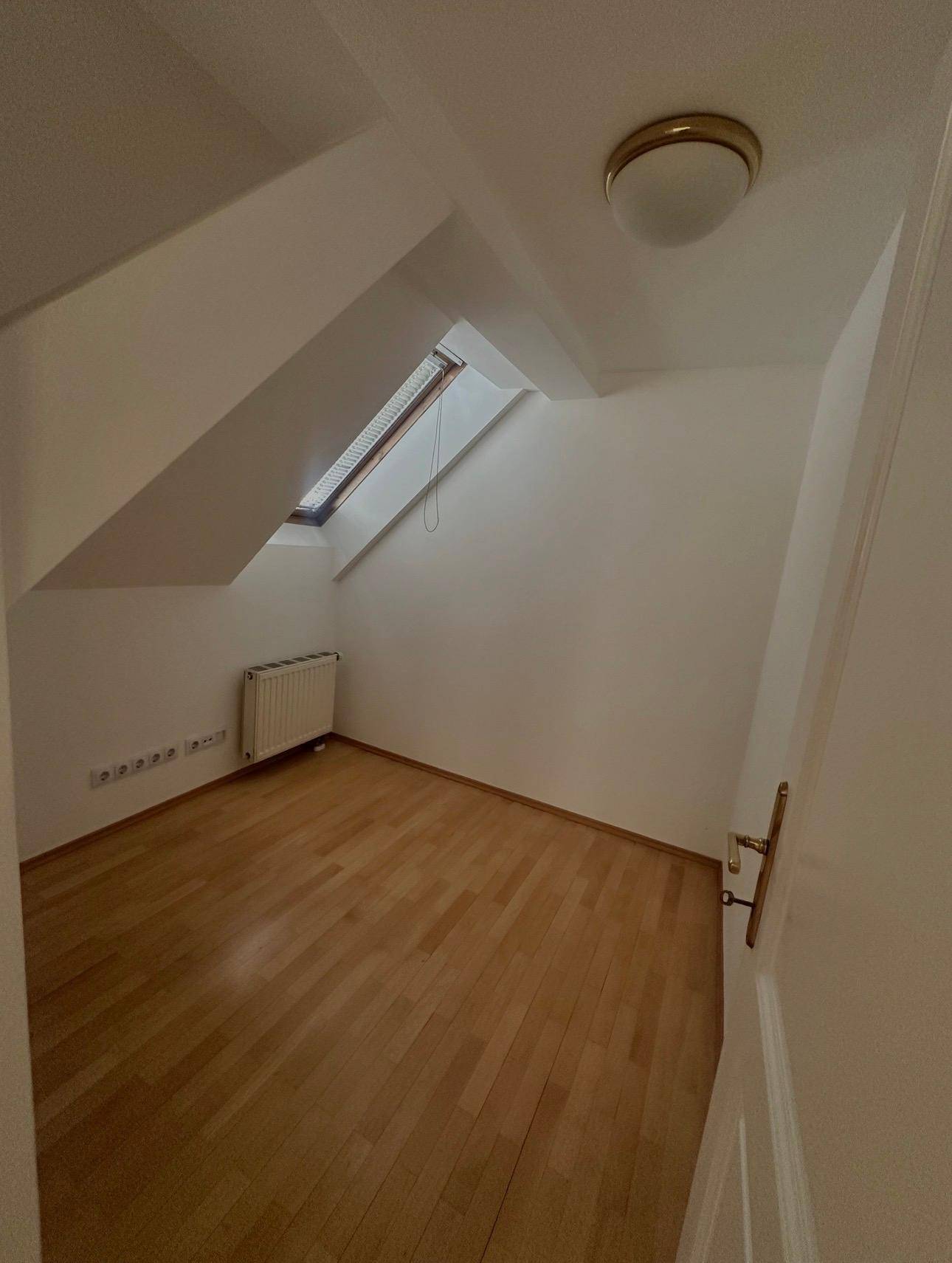 Kleines Zimmer mit Holzboden, Dachschräge und Dachfenster.
