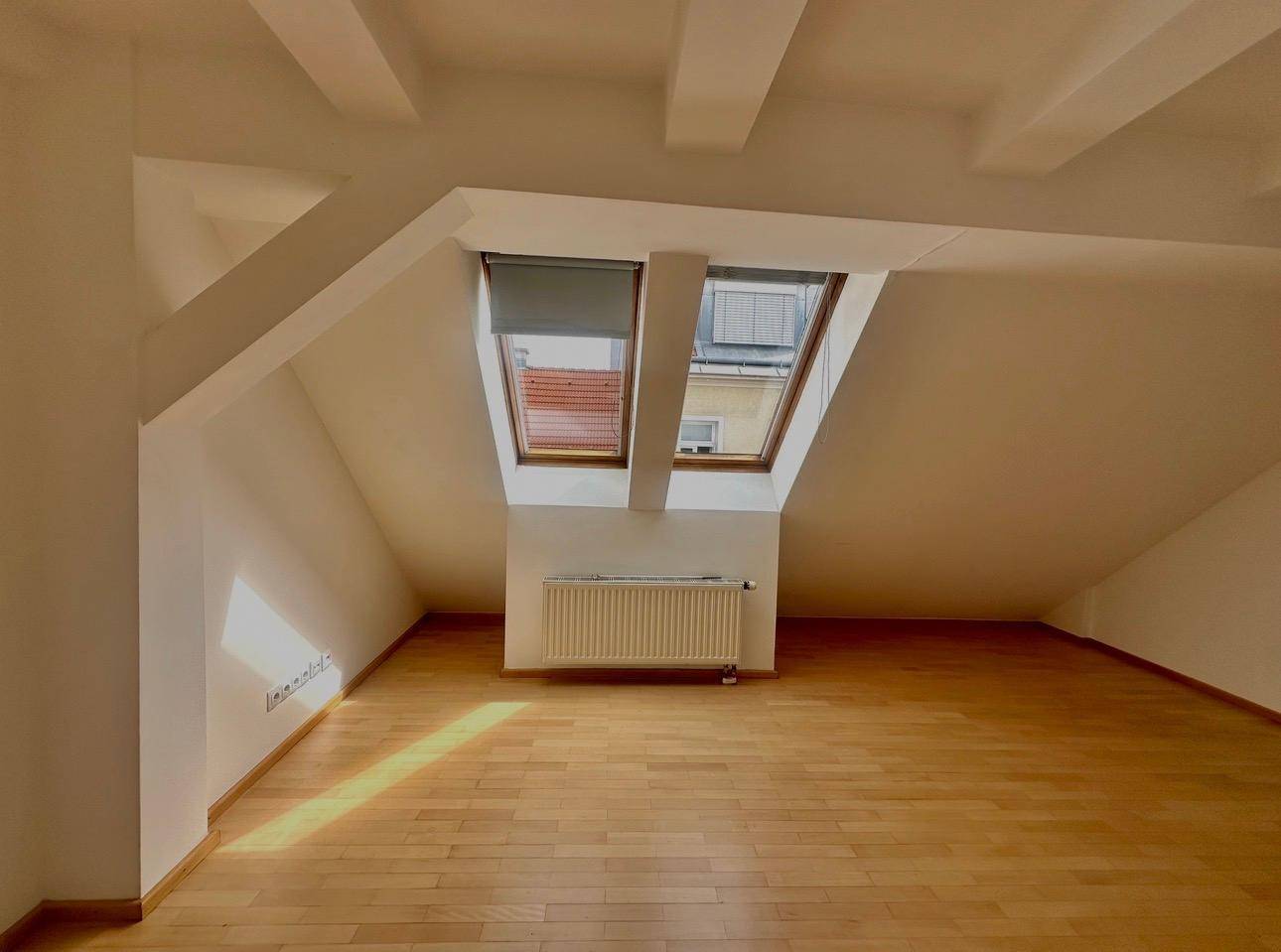 Heller Raum mit Holzboden, Dachschräge und zwei Dachfenstern.