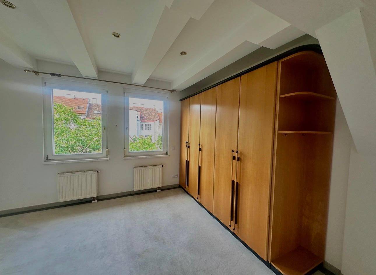 Schlafzimmer mit Einbauschränken, Holzboden und Blick ins Grüne.