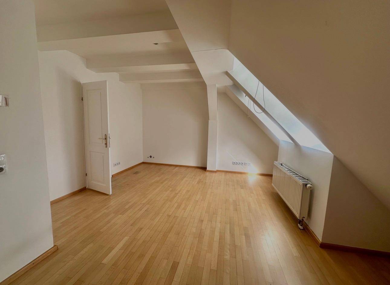Geräumiges Zimmer mit Holzboden, Dachschräge und weiß gestrichenen Wänden.