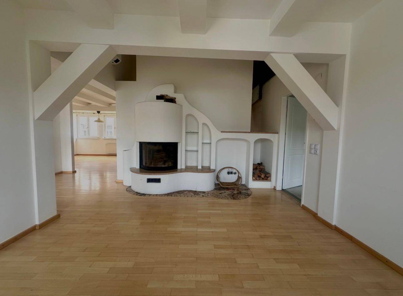 Offener Wohnbereich mit Kamin, Holzboden und sichtbaren Deckenbalken.