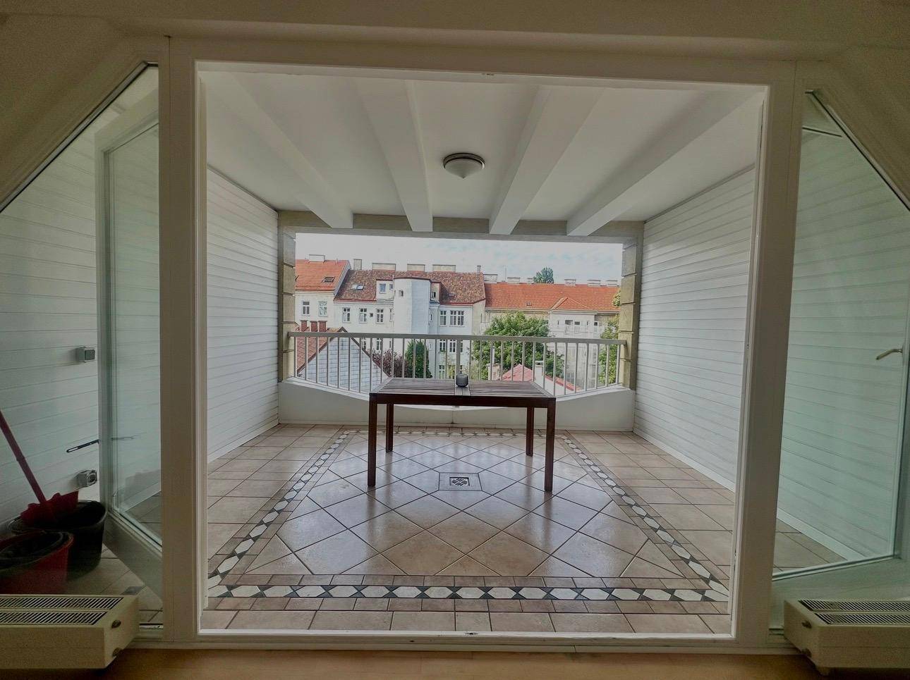 Überdachte Loggia mit Fliesenboden, Holzwänden und Stadtblick.