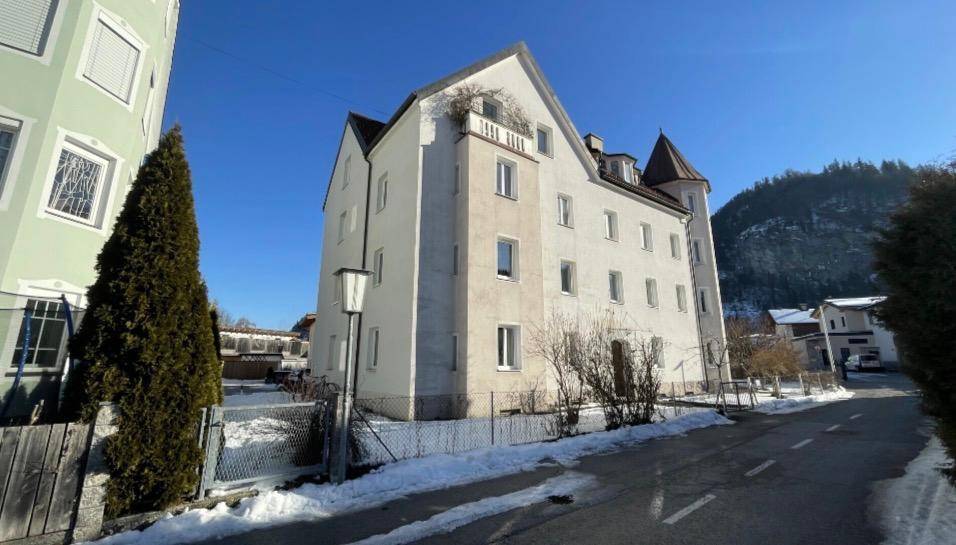 Mehrstöckiges Gebäude mit traditioneller Architektur in verschneiter Berglandschaft unter blauem Himmel.