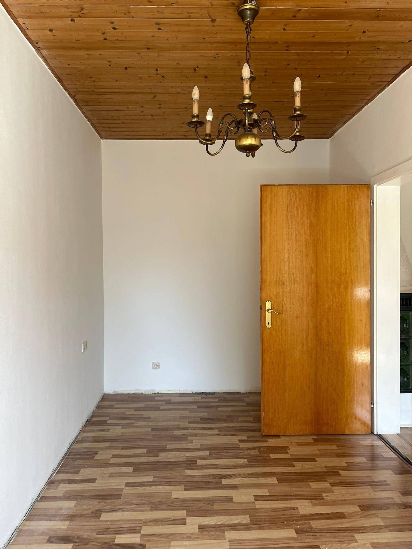 Leerer Raum mit Holzdecke, Laminatboden und einer Holztür, bereit zur individuellen Gestaltung.