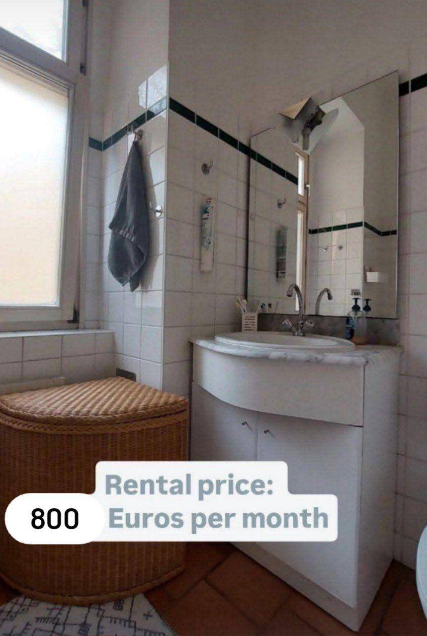 Badezimmer mit Waschbecken, Spiegel und Fenster, ausgestattet mit Fliesen und Terrakottaboden.