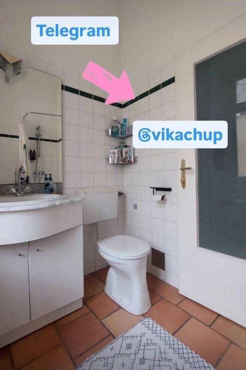 Badezimmer mit Toilette, Waschbecken und Spiegel, mit Terrakottaboden und Fliesen im 80er-Jahre-Stil.