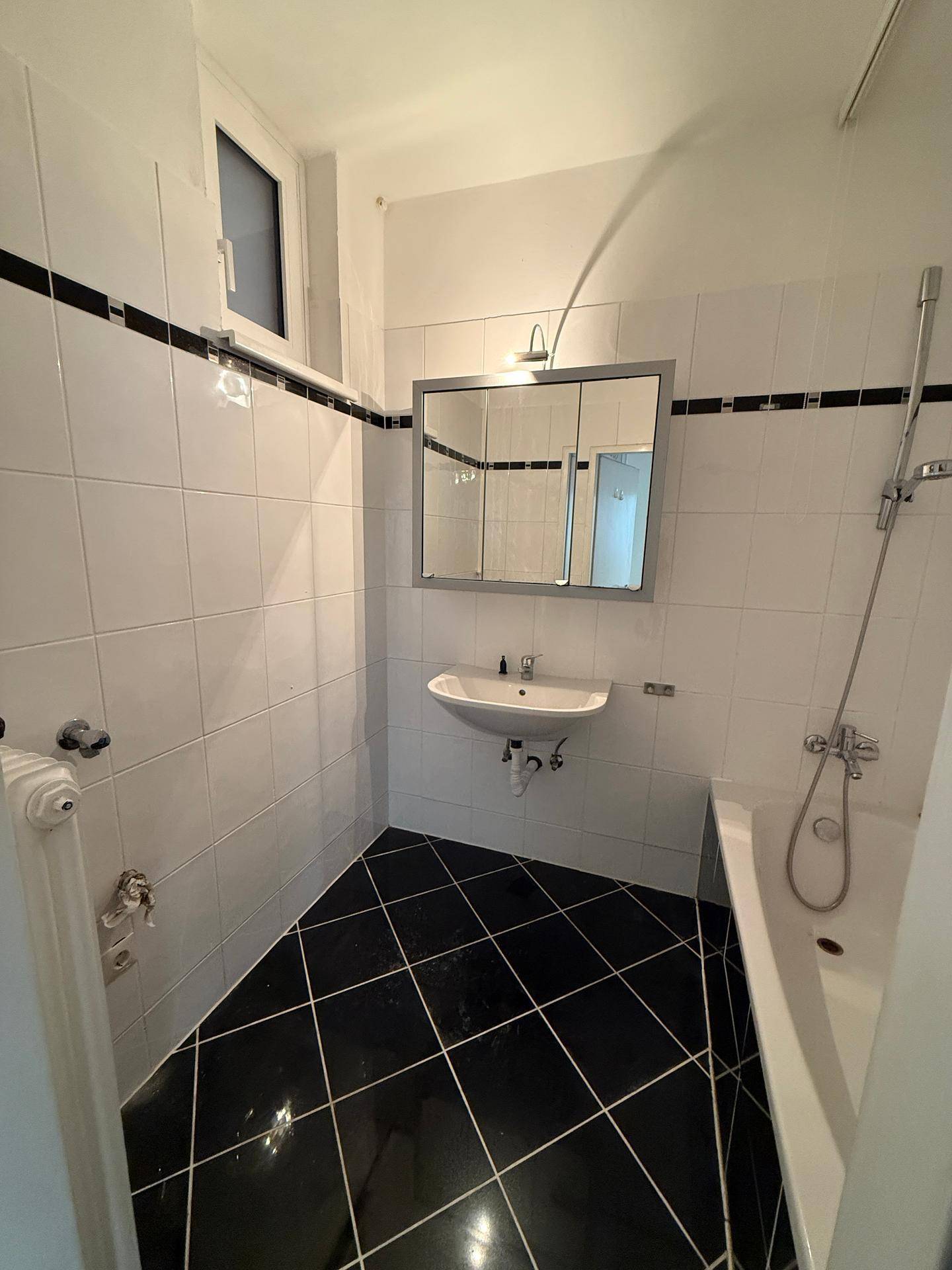 Badezimmer mit schwarz-weißen Fliesen, Badewanne, Waschbecken und Spiegelschrank.