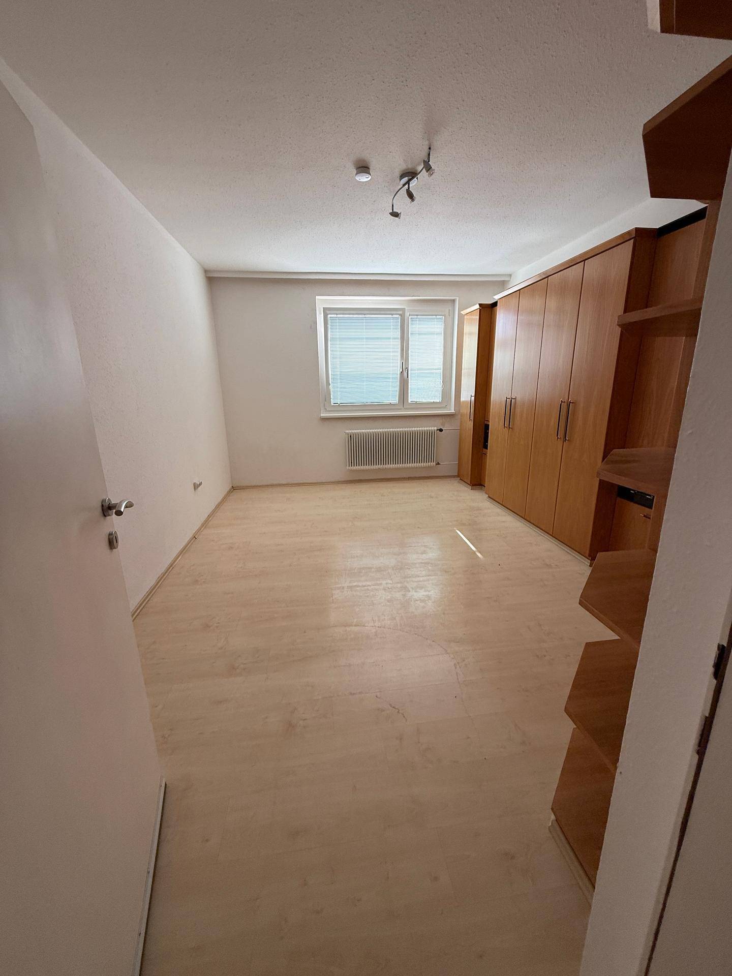Helles Schlafzimmer mit Laminatboden, großem Kleiderschrank und Fenster für natürliche Belichtung.