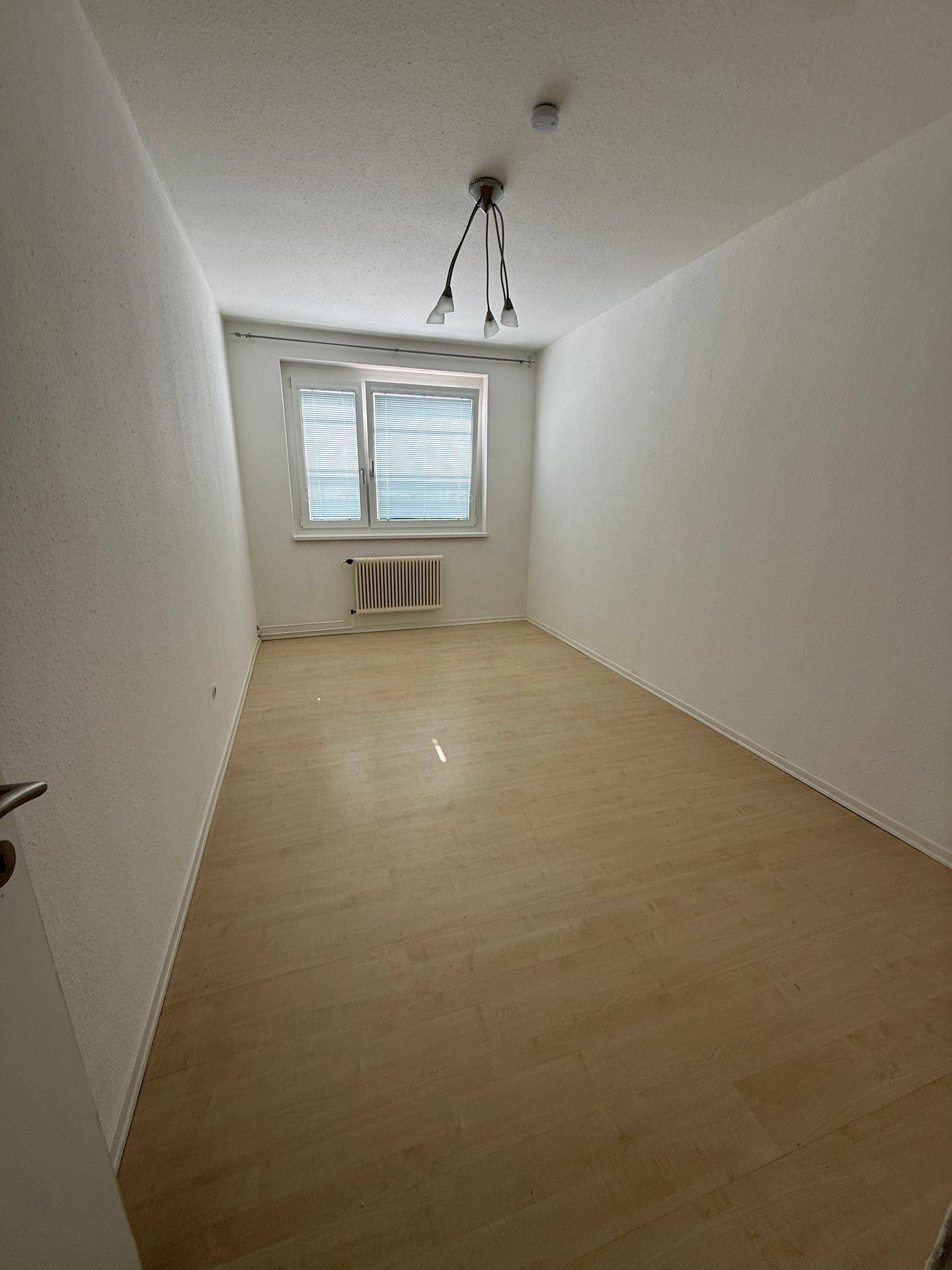 Unmöbliertes Schlafzimmer mit hellem Laminatboden und einem Fenster, bereit zur individuellen Gestaltung.