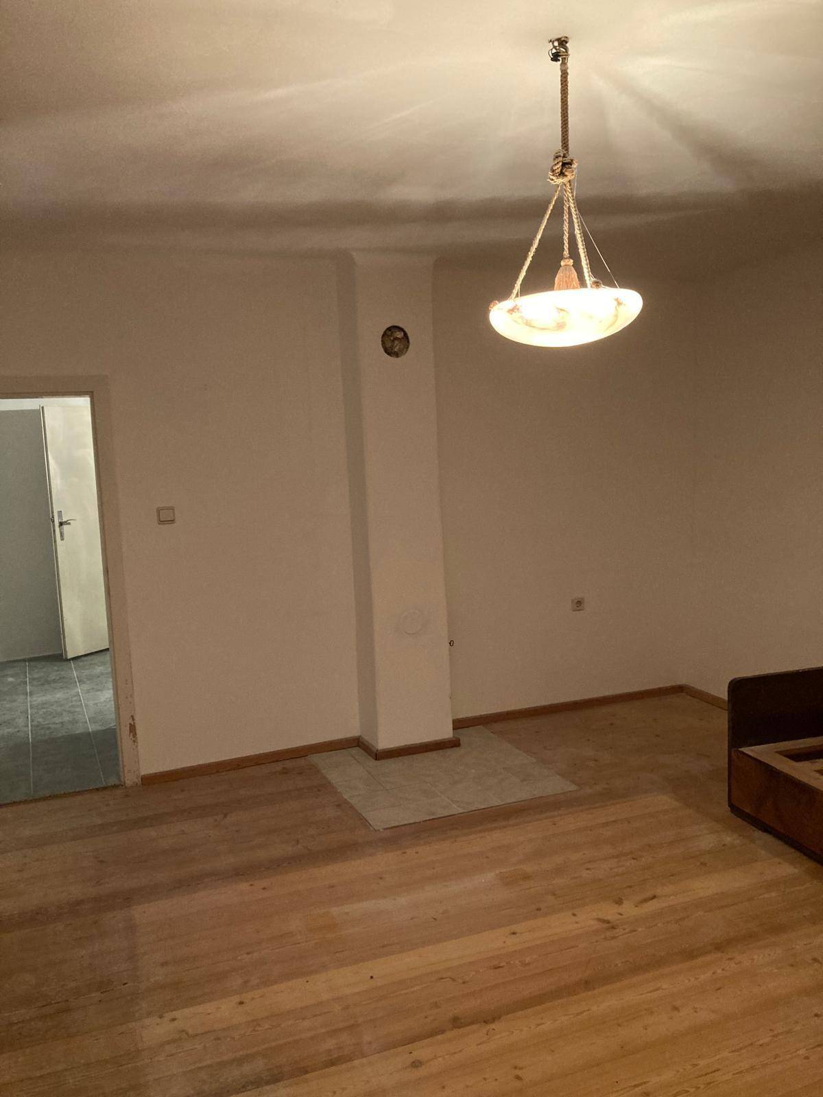 Heller Raum mit Holzfußboden und einer Deckenlampe, der auf die Einrichtung wartet.