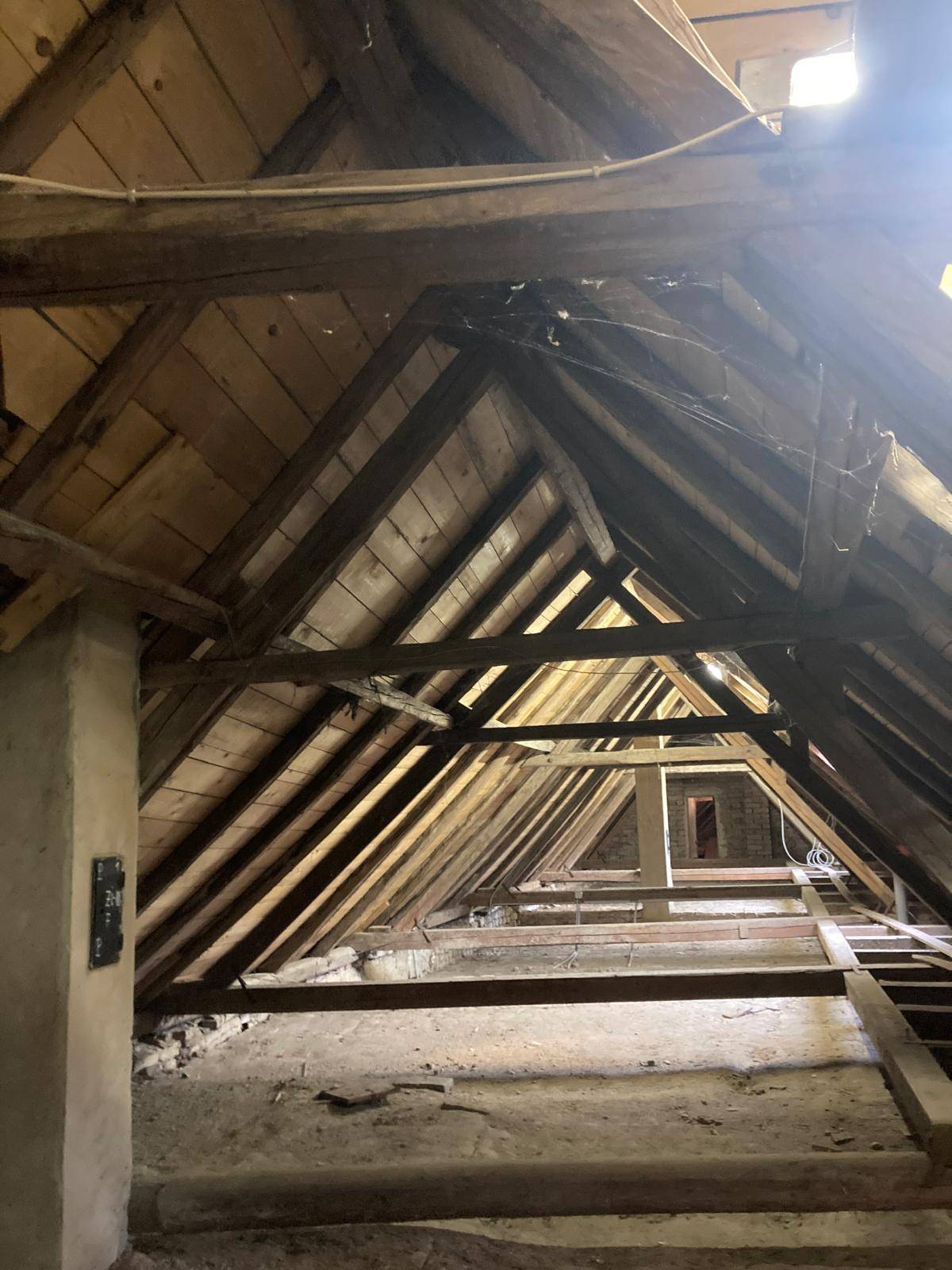 Dachboden mit sichtbaren Holzbalken und Dachschrägen, der den ursprünglichen Zustand des Gebäudes zeigt.