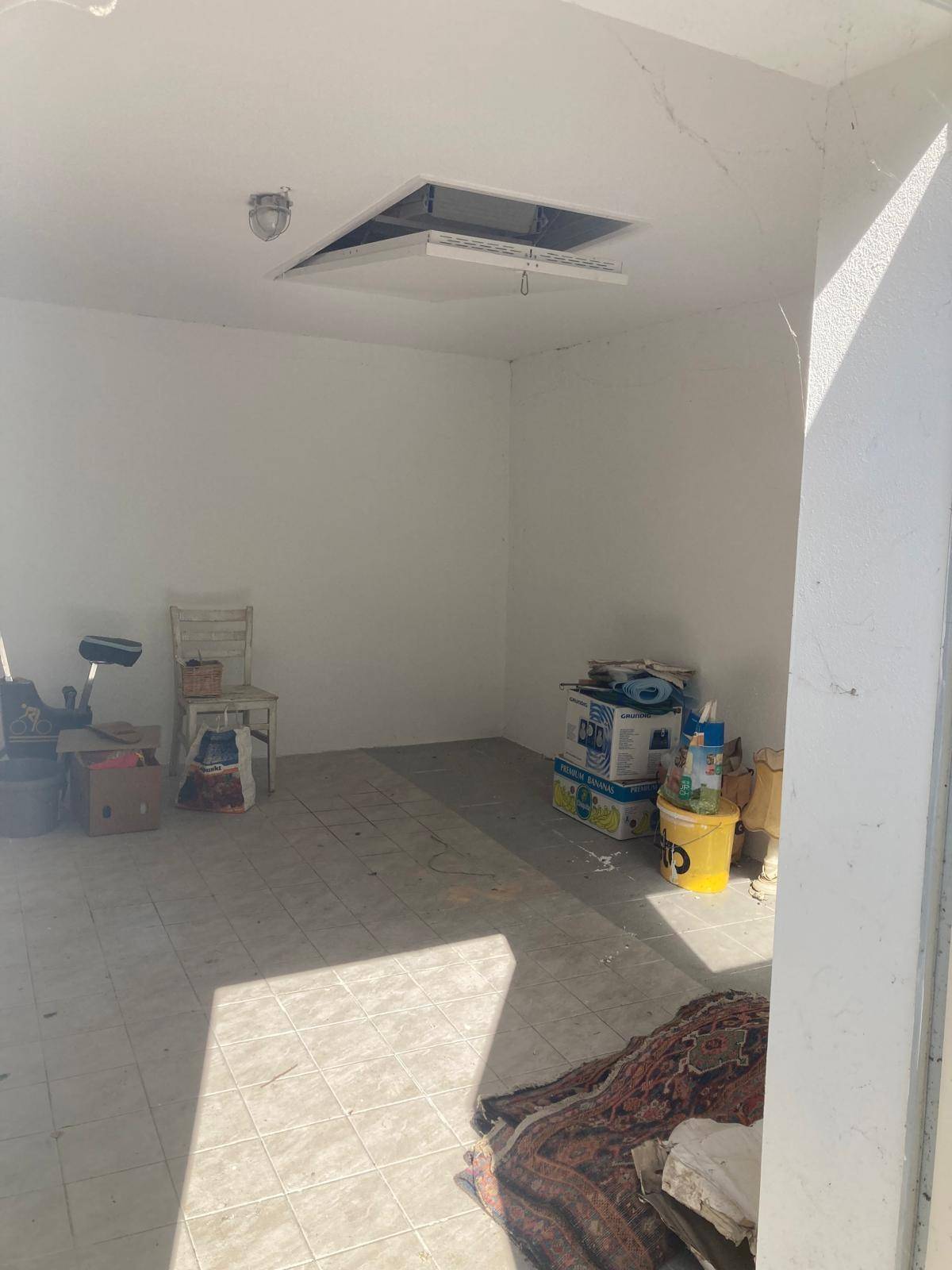Geräumiger leerer Raum mit Fliesenboden und einem Zugang zum Dachboden, ideal als Garage oder Abstellraum.