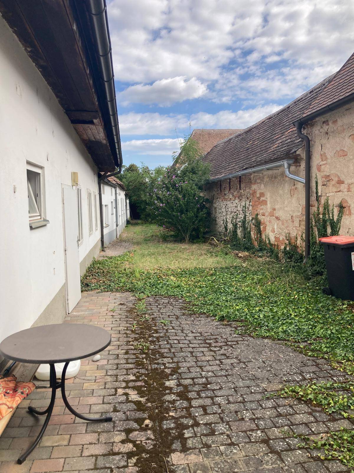 Hinterhof mit gepflastertem Weg, viel Grün und einem kleinen Tisch mit Stühlen für den Außenbereich.