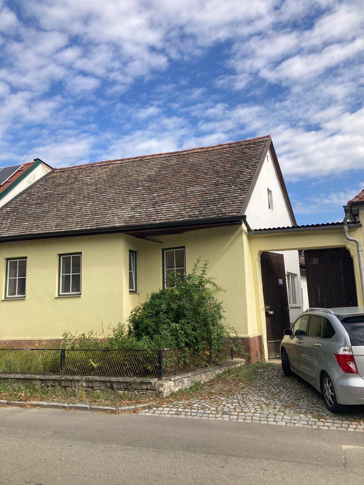 Ein gelbes Haus mit braunem Dach und einem Garagentor, davor ein geparktes Auto.