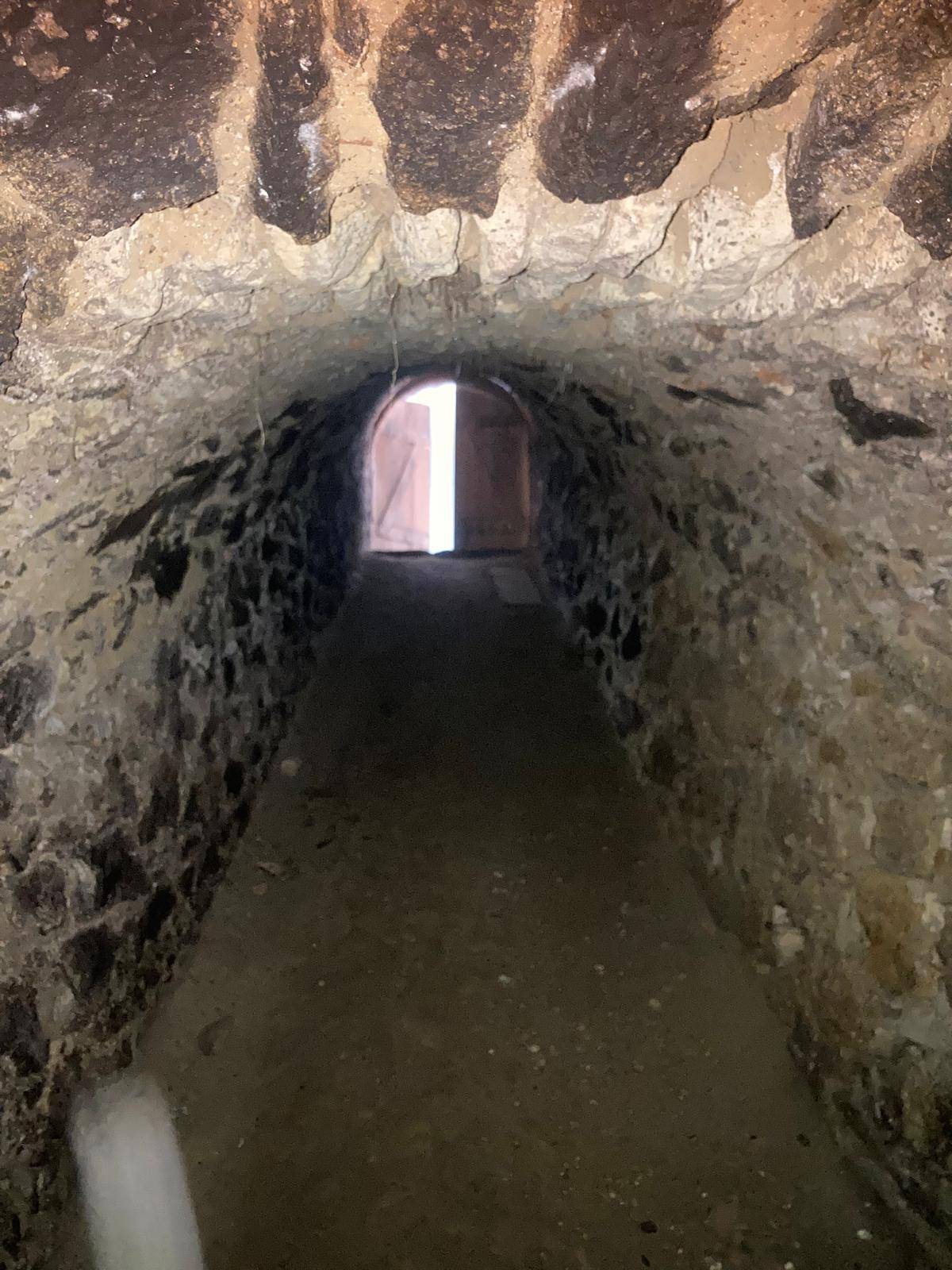 Alter Gewölbekeller mit robusten Steinwänden und einem Durchgang, der Licht am Ende zeigt.