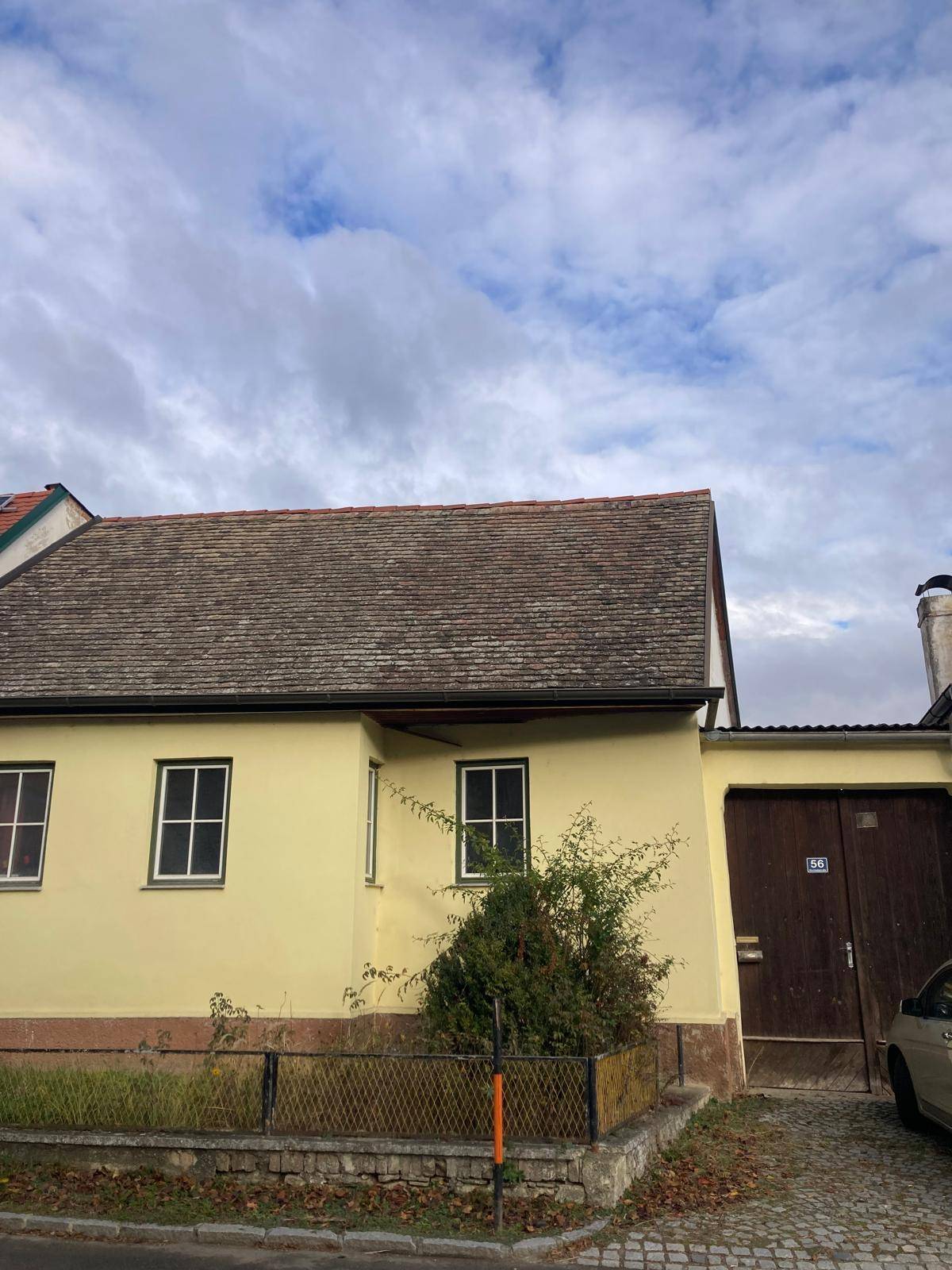 Ein gelb gestrichenes Haus mit traditionellem Dach und einem großen Holztor, umgeben von Vegetation.