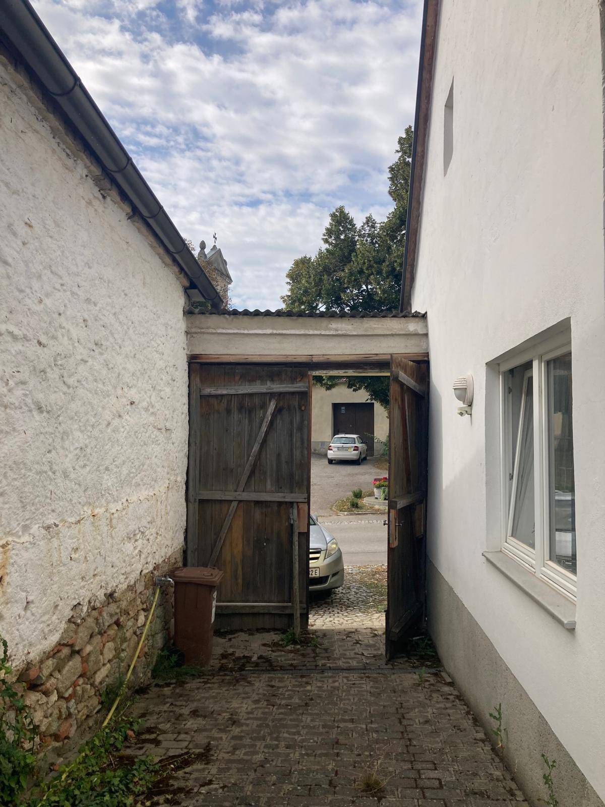 Einfahrt mit einem rustikalen Holztor und Blick auf die Straße, umgeben von alten Gebäuden.