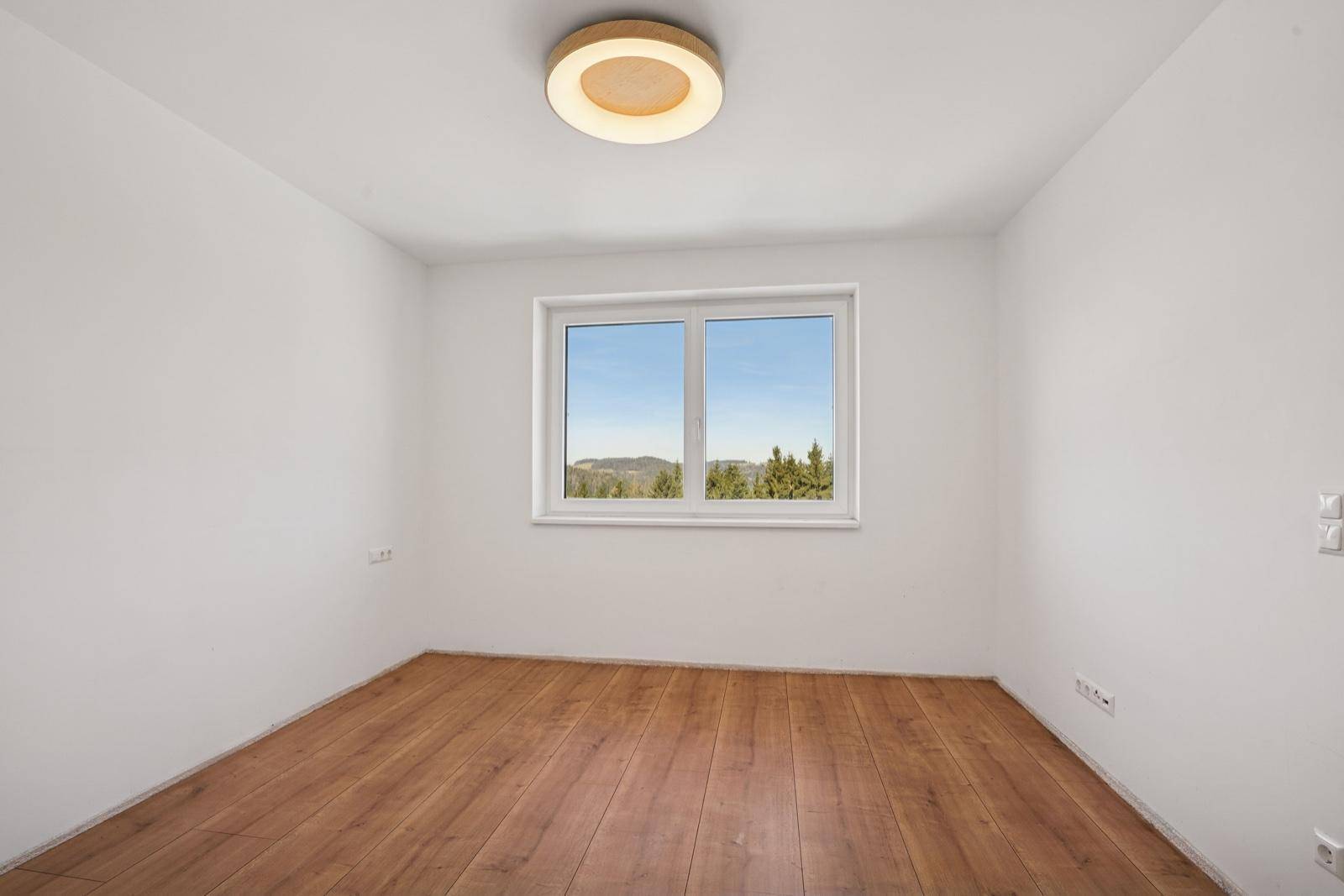 Helles Schlafzimmer mit Holzboden und weitem Blick in die Natur.