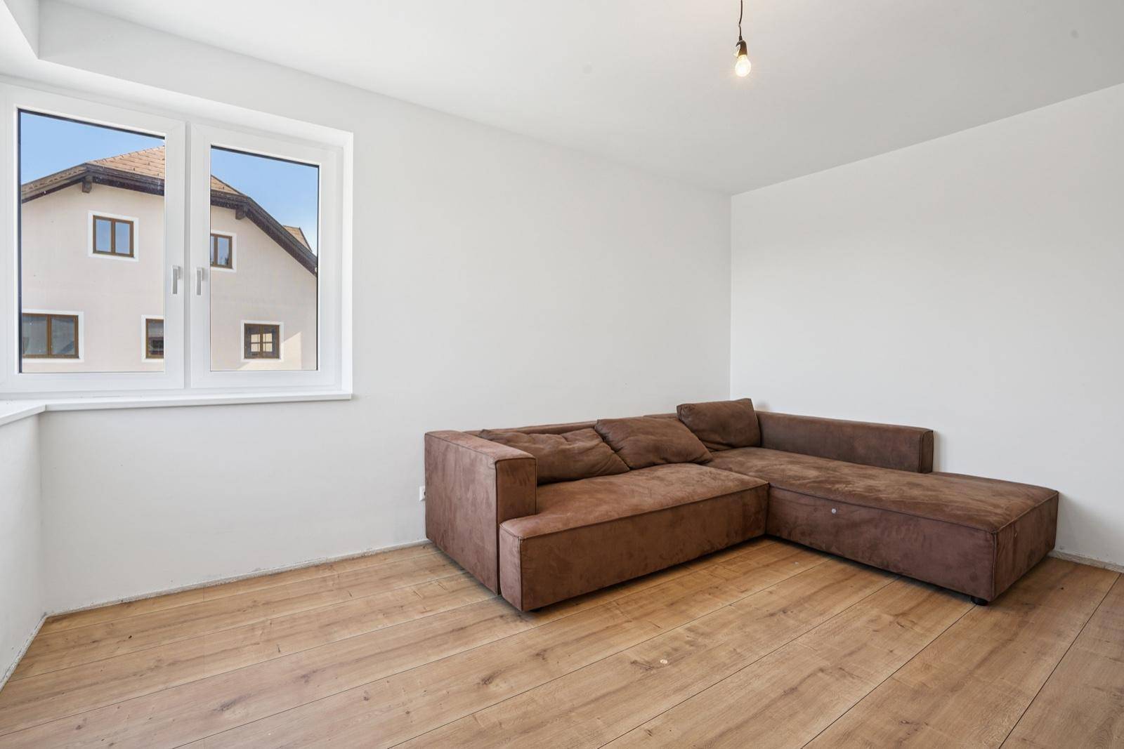 Gemütliches Wohnzimmer mit Holzboden und großem Ecksofa, hell durch das Fenster.