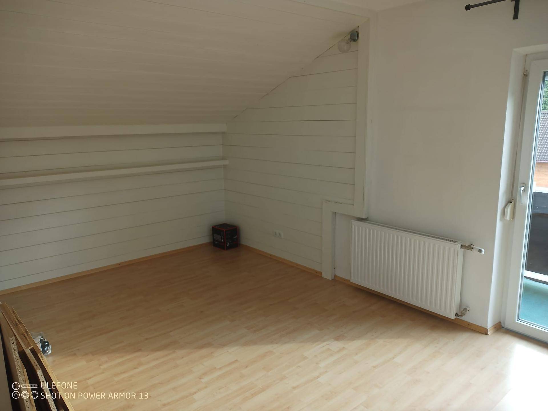 Dachgeschosszimmer mit Holzverkleidung, Laminatboden und Zugang zu einem Balkon.